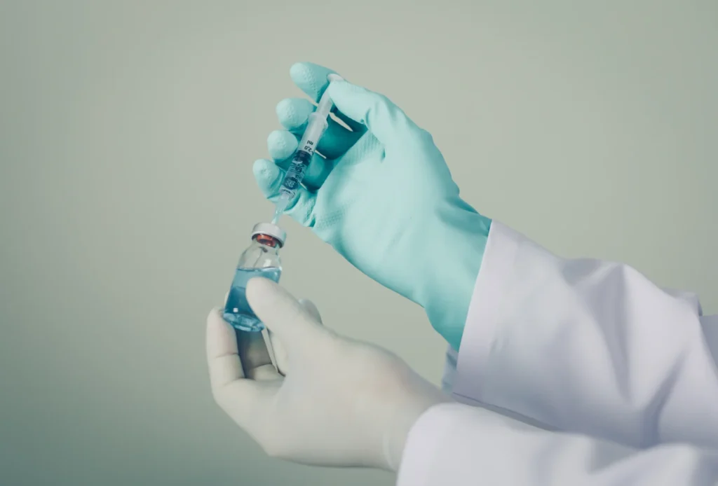Mãos com luvas preparando uma seringa a partir de um frasco de medicamento (imagem ilustrativa)